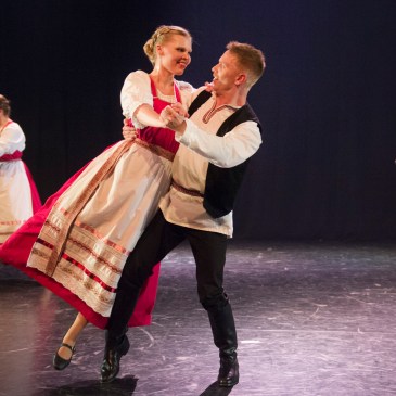 Perinteisiin, kansanomaisiin esiintymisasuihin pukeutunut tanssipari hymyilee toisilleen kesken noston.