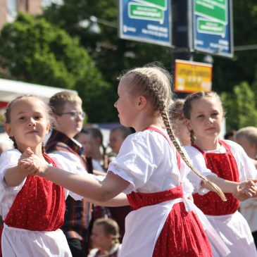 Nuoret kansantanssijat esiintyvät aurinkoisessa säässä torilla.